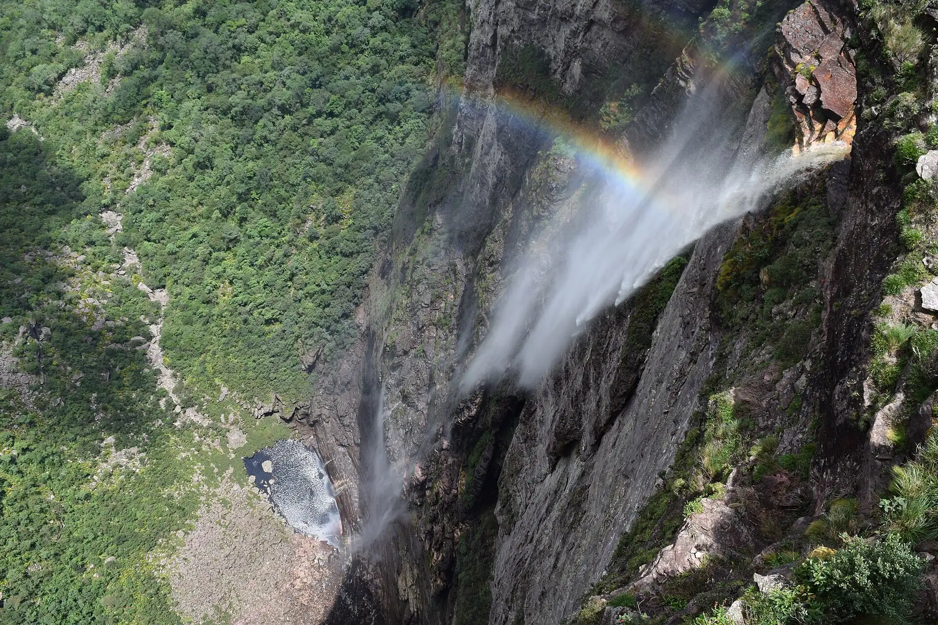 Cachoeira da Fumaça vista do alto, com a água se dispersando em névoa e um arco-íris no paredão da Chapada Diamantina