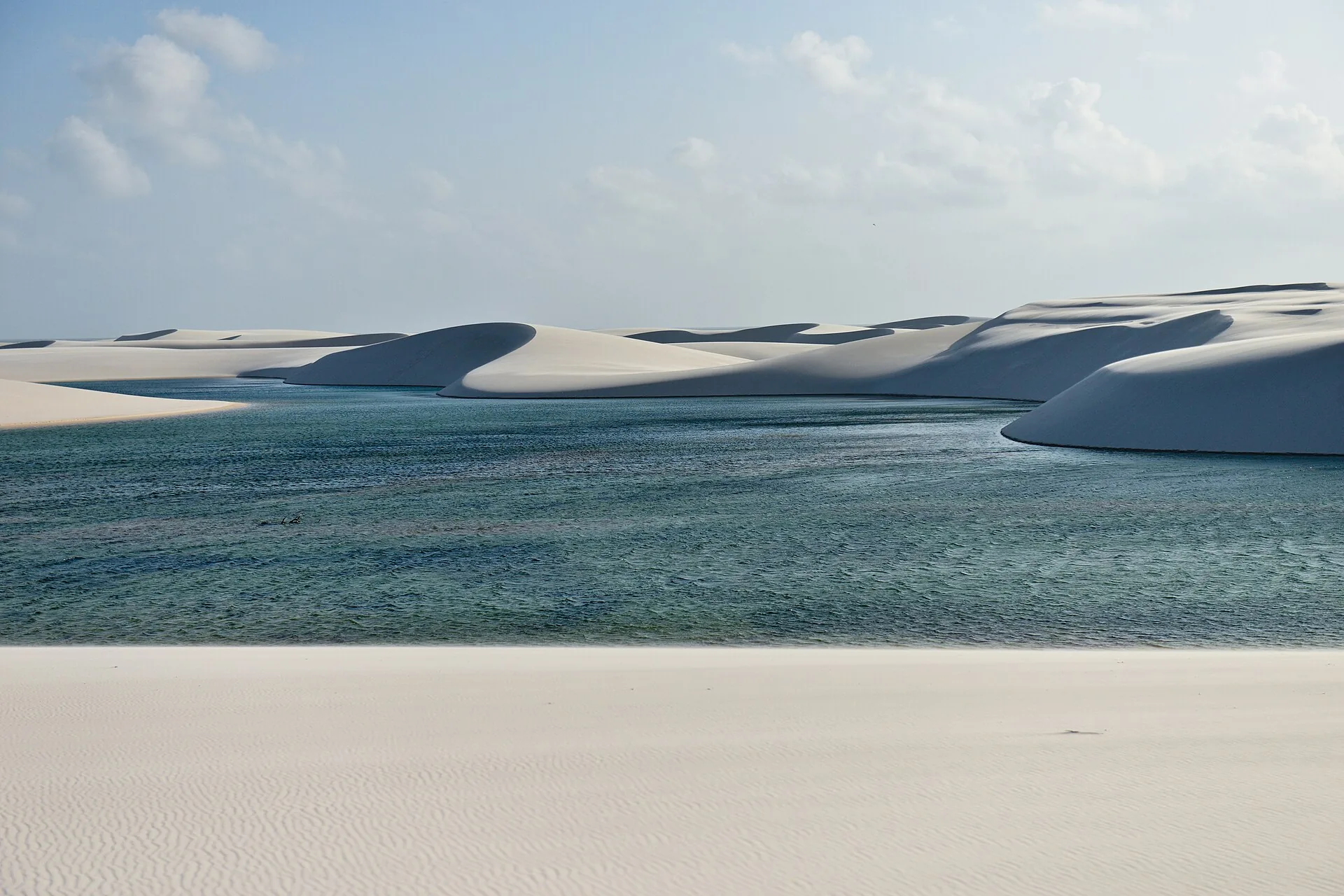 Lagoa de água esverdeada entre dunas de areia branca nos Lençóis Maranhenses