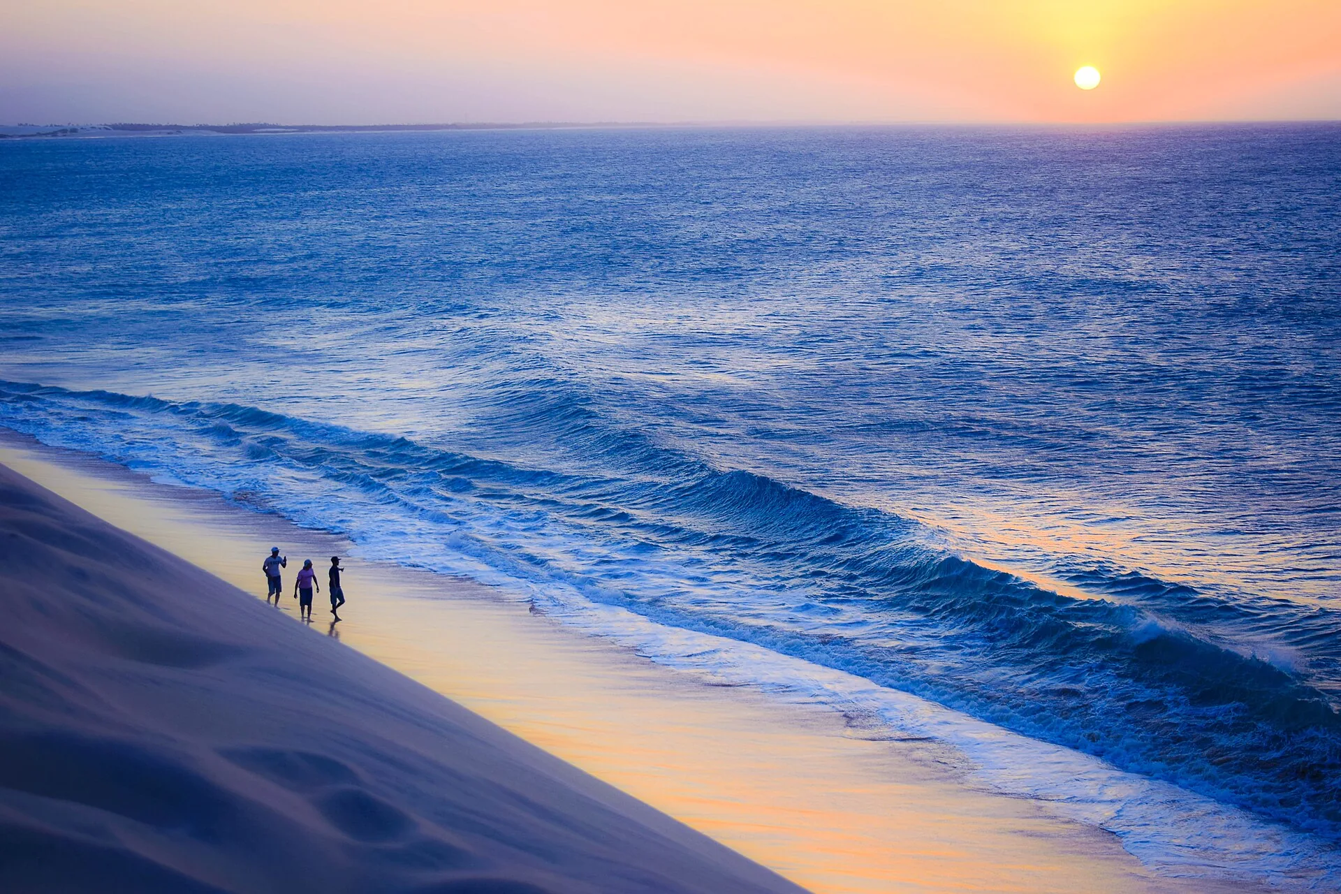 Duna do Pôr do Sol em Jericoacoara, com o mar ao fundo e três silhuetas caminhando na areia