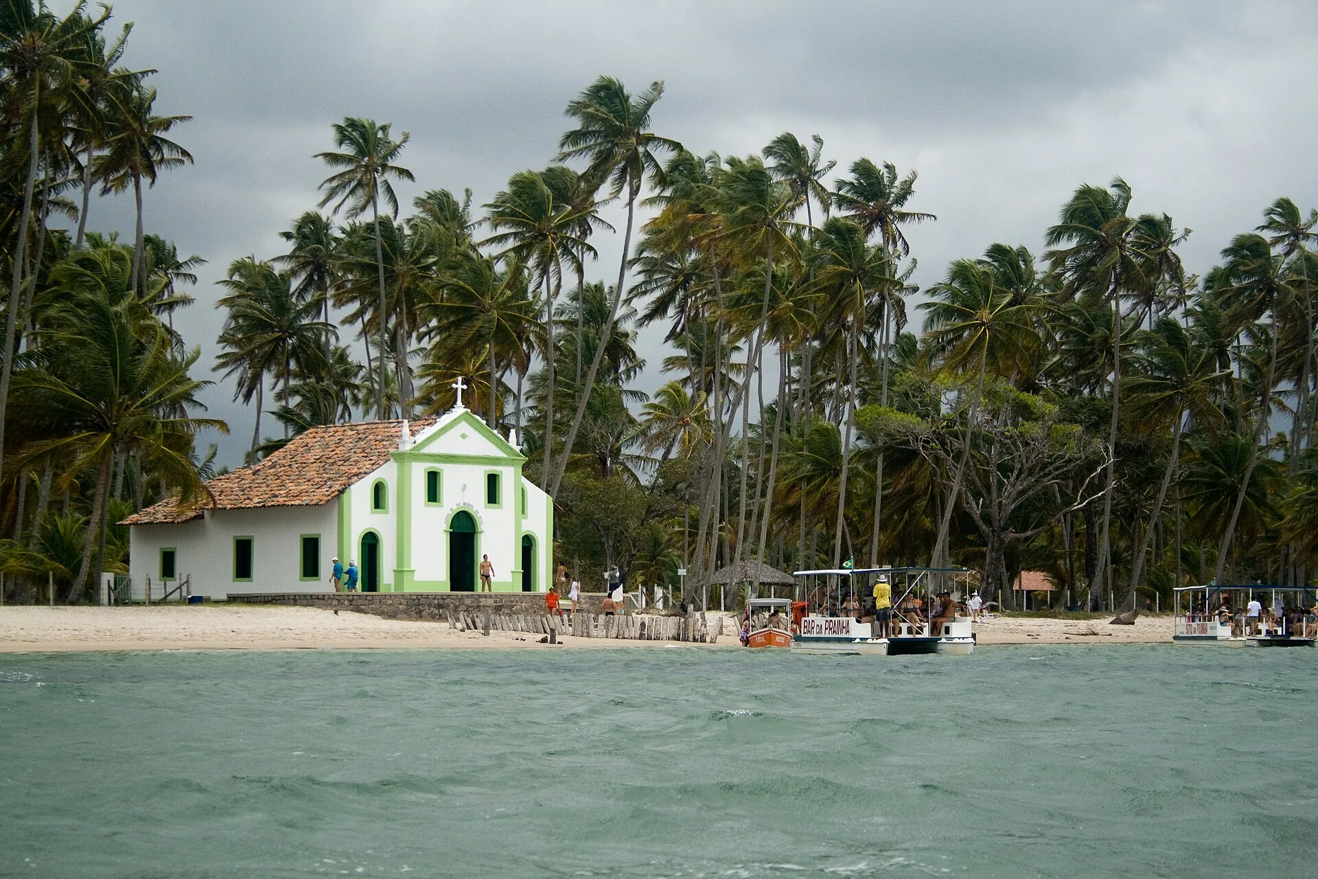 Capela branca na Praia dos Carneiros, em Pernambuco, cercada de coqueiros, vista do mar