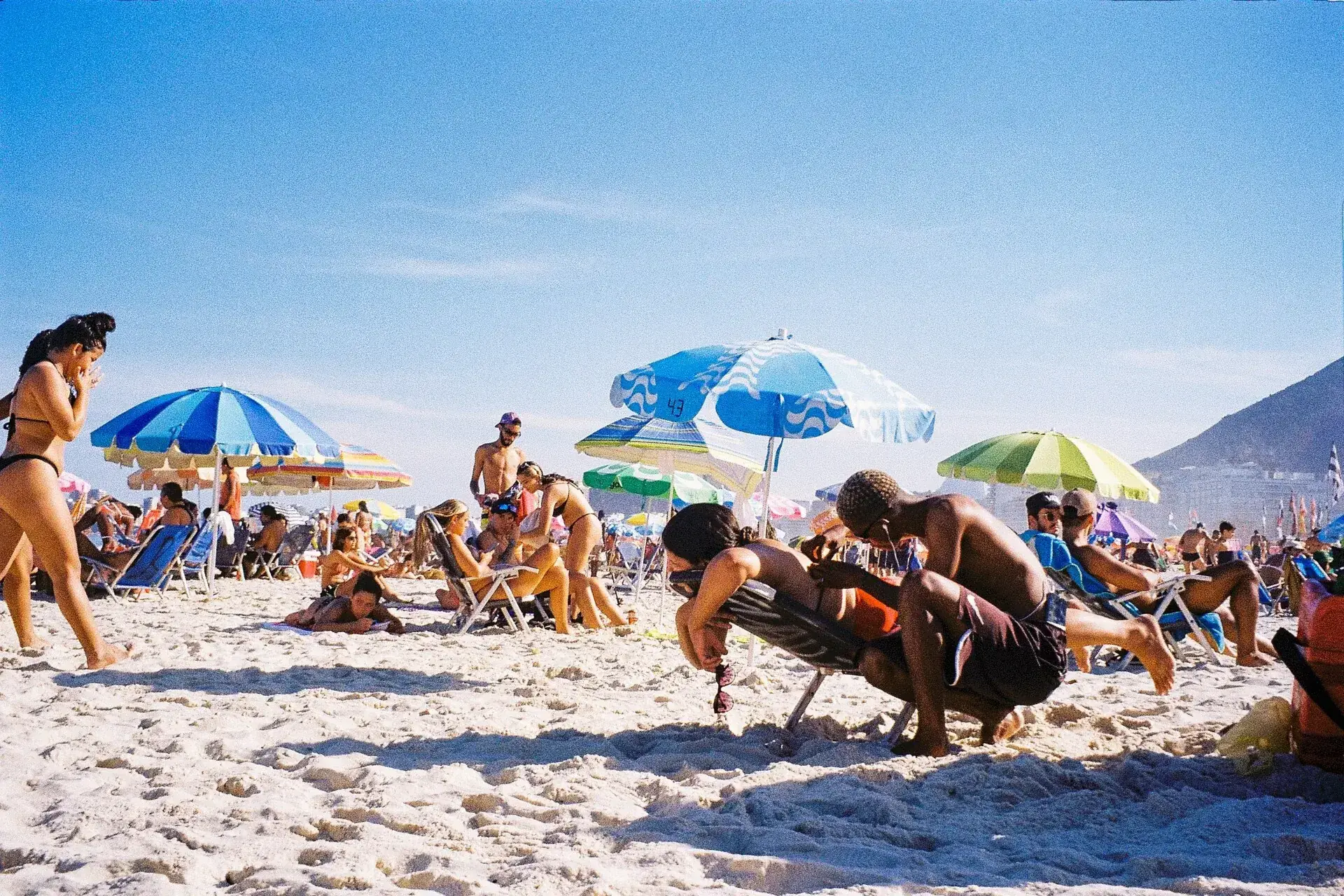 Praia brasileira cheia de banhistas e guarda-sóis coloridos em dia de alta temporada