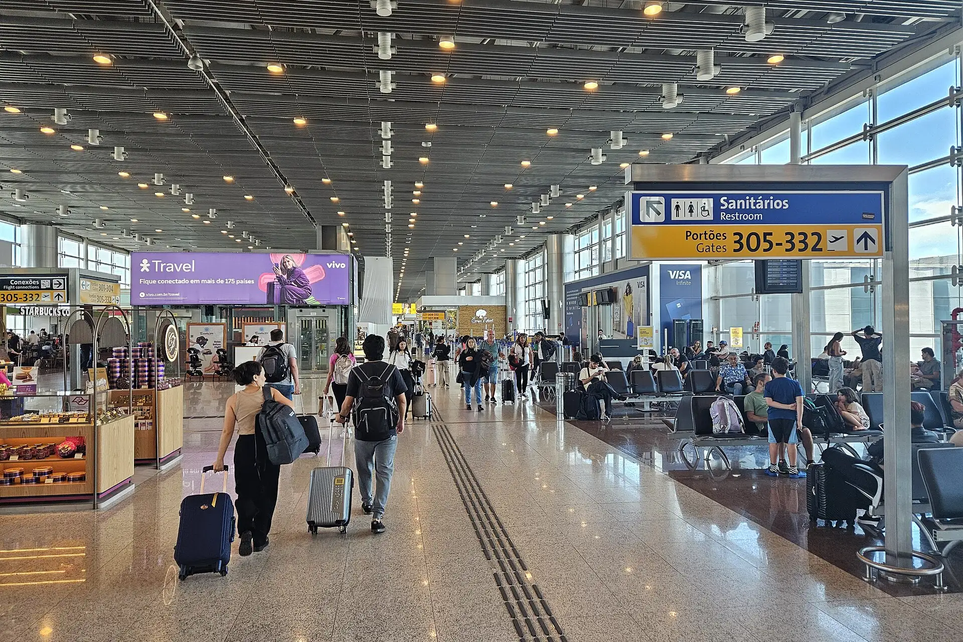 Saguão de embarque do Terminal 3 de Guarulhos, com passageiros caminhando e área de espera ao fundo